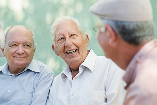 Three senior men talking and smiling, one with his back to the camera and out of focus