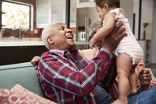 Elderly grandfather holding infant grandchild up in the air smiling