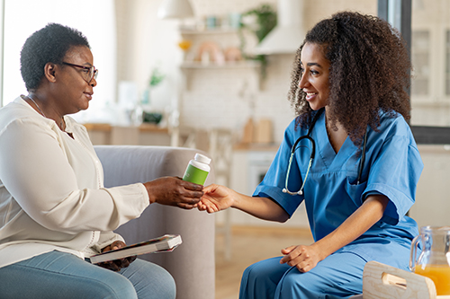 Young nursing handing elderly woman a bottle of vitamins