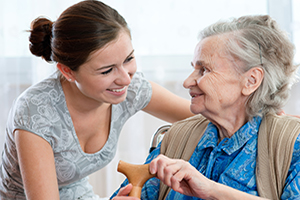 You woman with hear in a bun smiling at senior woman sitting down with hands on her cane